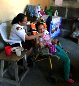 Dayana in a wheelchair with her mother holding her cup
